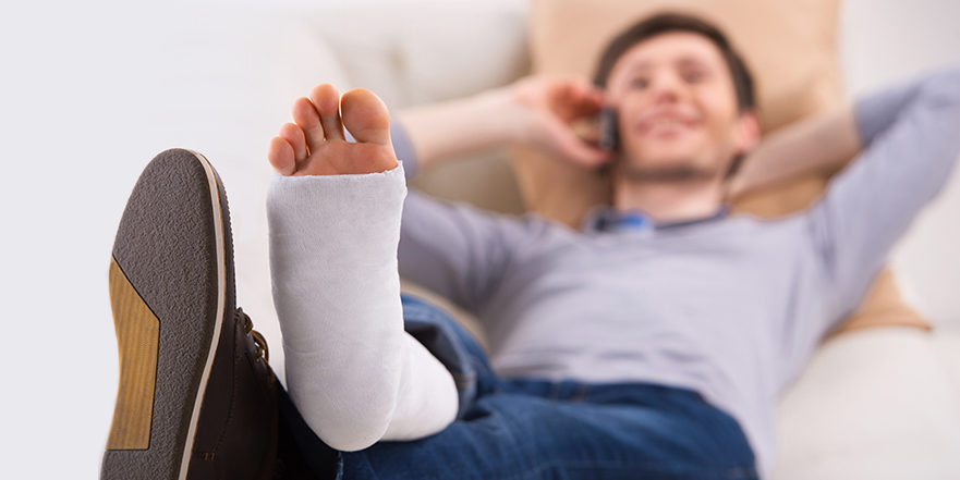 Man lying back talking on the phone with bandaged foot elevated