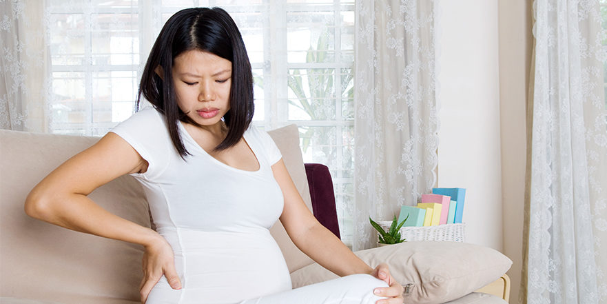 Pregnant woman sittign on couch holding back in pain